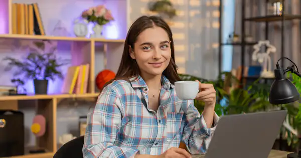 Trabajadora autónoma sonriendo con un café frente a su portátil en casa
