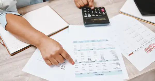 Manos revisando documentos de pagos junto a una calculadora sobre la mesa