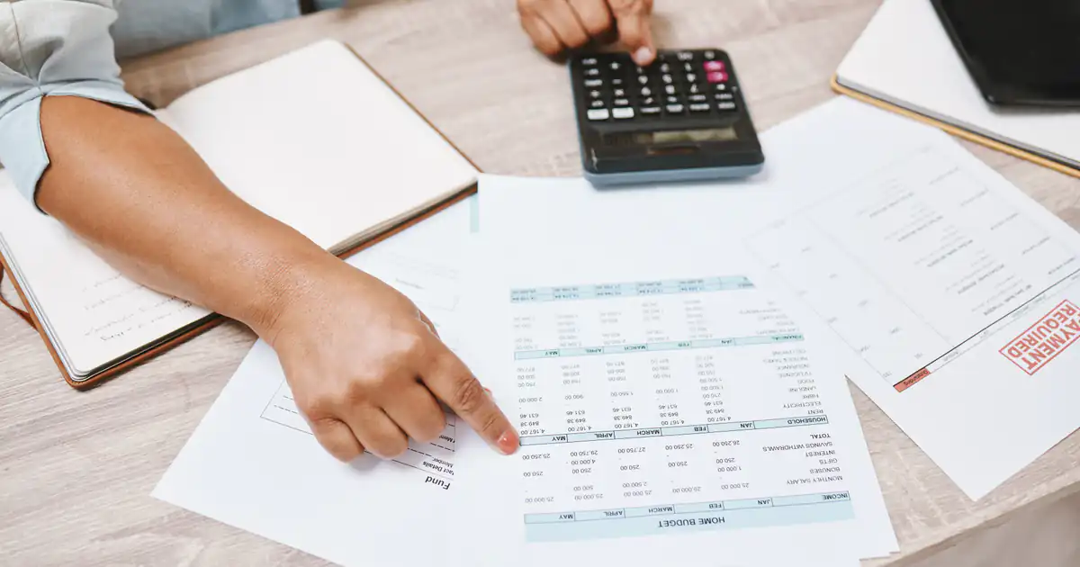 Manos revisando documentos de pagos junto a una calculadora sobre la mesa