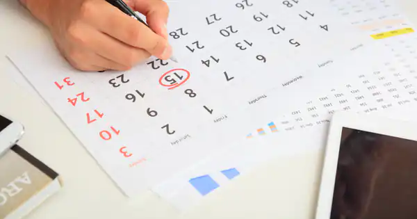 Mano marcando fechas en un calendario de papel con un bolígrafo
