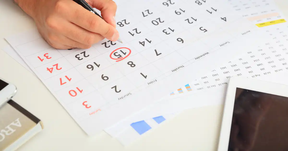 Mano marcando fechas en un calendario de papel con un bolígrafo