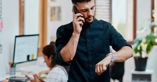 Empleado hablando por teléfono mientras mira el reloj en la oficina