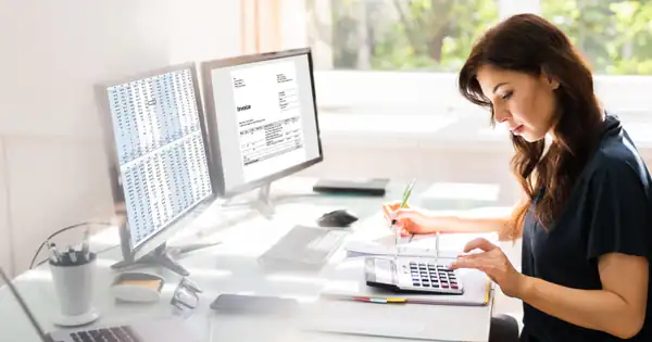 Asesora trabajando con dos monitores y calculadora en su despacho