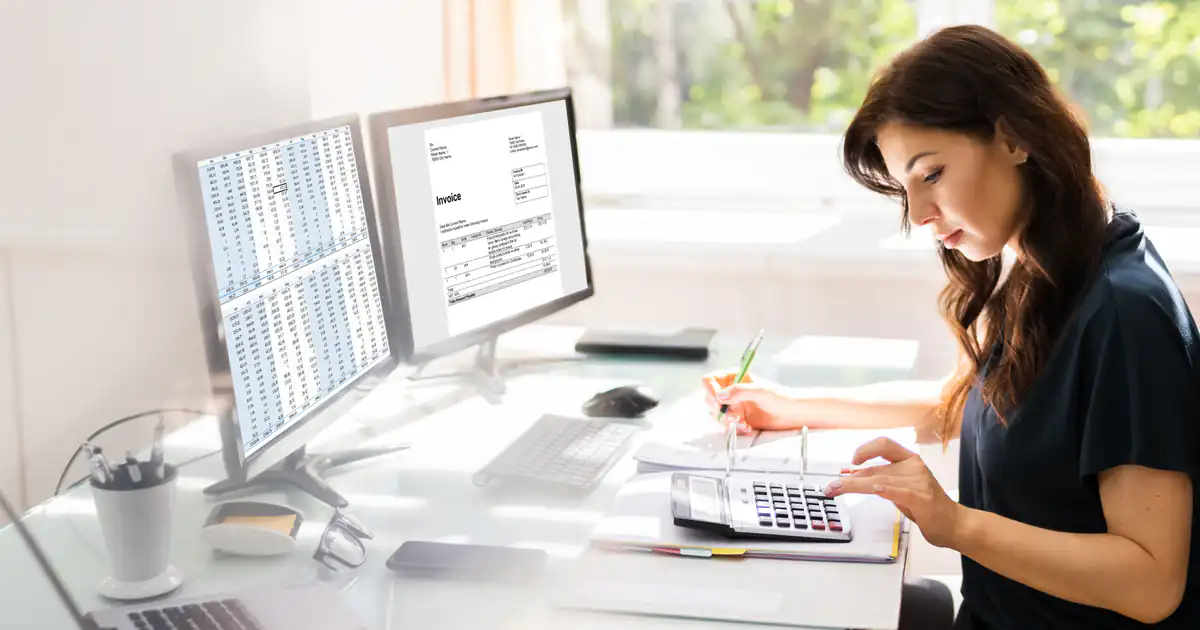 Asesora trabajando con dos monitores y calculadora en su despacho