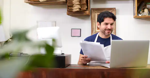 Dueño de un comercio revisando facturas junto a su portátil