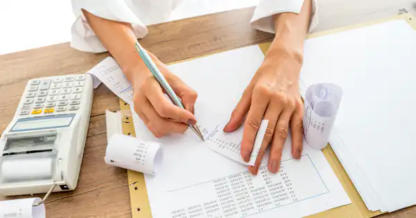 Manos corrigiendo un documento junto a una calculadora con ticket