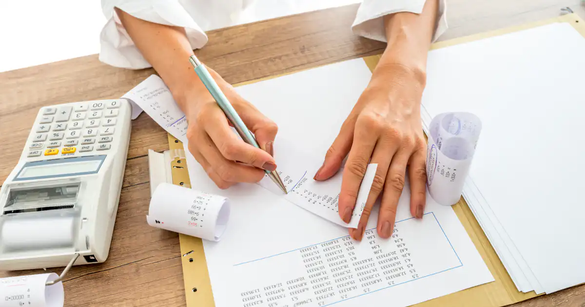 Manos corrigiendo un documento junto a una calculadora con ticket