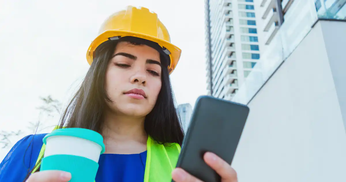 Trabajadora con casco consultando su móvil en el exterior