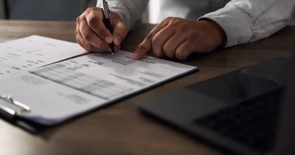 Manos revisando una factura impresa con bolígrafo sobre la mesa