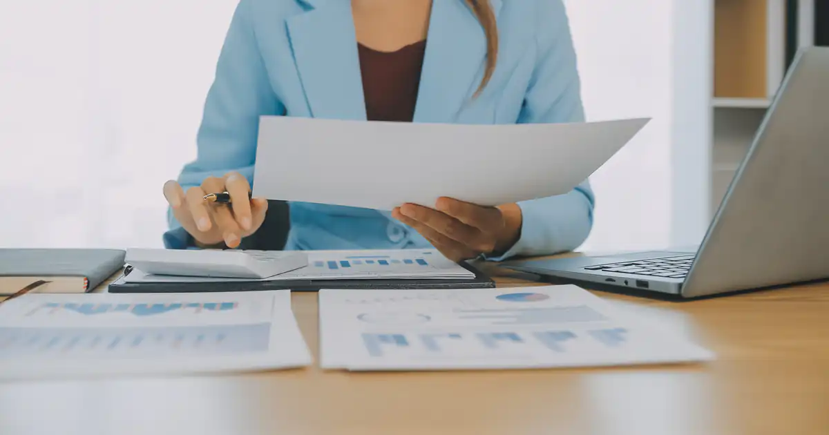 Empresaria revisando informes financieros junto a su portátil