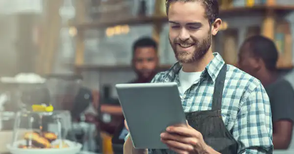 Dueño de una cafetería sonriendo mientras usa una tableta