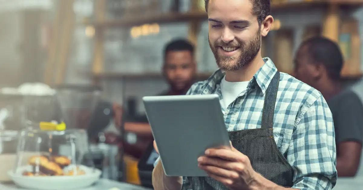 Dueño de una cafetería sonriendo mientras usa una tableta
