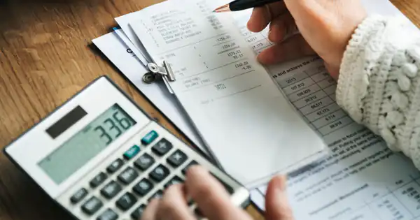 Manos anotando cifras junto a una calculadora y varios recibos
