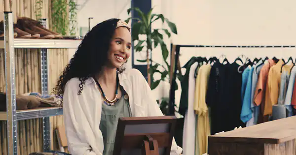 Dependienta sonriente atendiendo la caja de su tienda de ropa