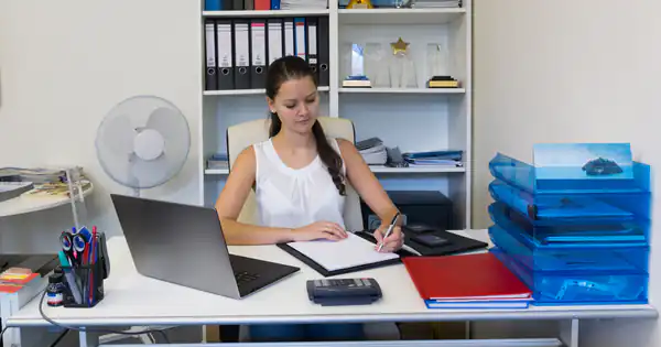 Trabajadora de un despacho rodeada de archivadores revisando papeles con calculadora