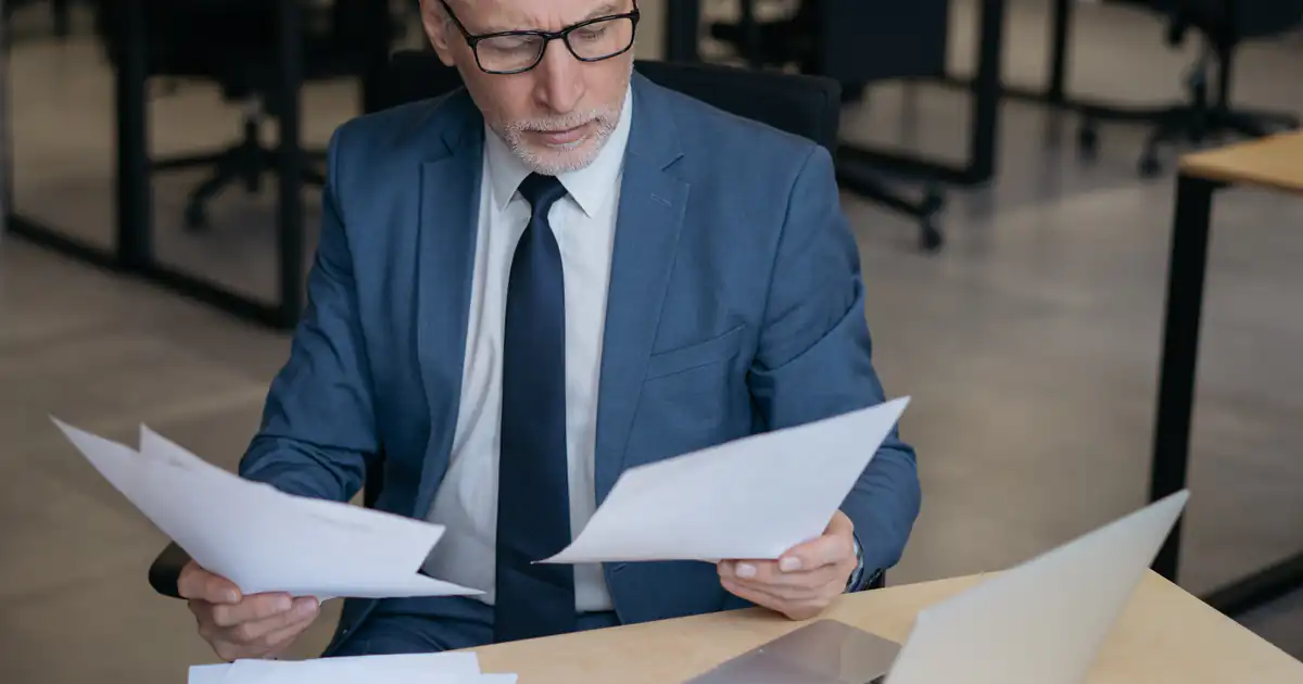 Empresario con gafas leyendo documentos con preocupación en su oficina